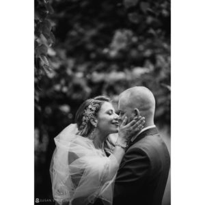 A black and white photo of a bride and groom kissing at their wedding.