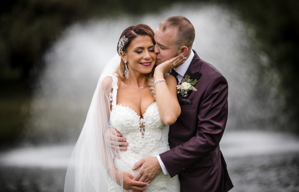 A bride and groom, amidst their wedding at Flowerfield Celebrations, sweetly embrace in front of a majestic fountain.