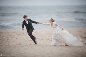 A bride and groom having their wedding at the Bridgehampton Tennis and Surf Club, joyfully running on the beach.