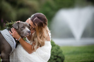 A bride is hugging her dog at a wedding at Flowerfield Celebrations in front of a fountain.