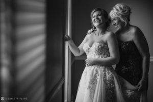 A bride and her mother, amidst the excitement of a wedding at the Berkeley Oceanfront Hotel, share a heartfelt moment while gazing out a window.