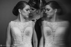 A bride is putting on her wedding dress in front of a mirror at Loews Hotel in Philadelphia.