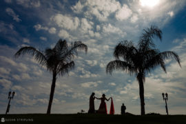 The ocean place resort bride and groom are silhouetted against the sky and palm trees.