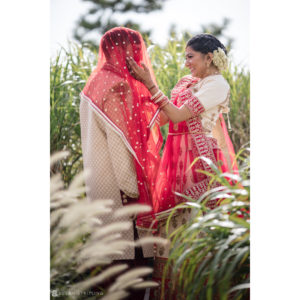 An Indian bride and groom standing in tall grass, surrounded by the serene beauty of an ocean place resort.