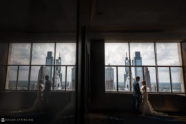 A bride and groom standing in front of a window overlooking the city at their Philadelphia wedding.