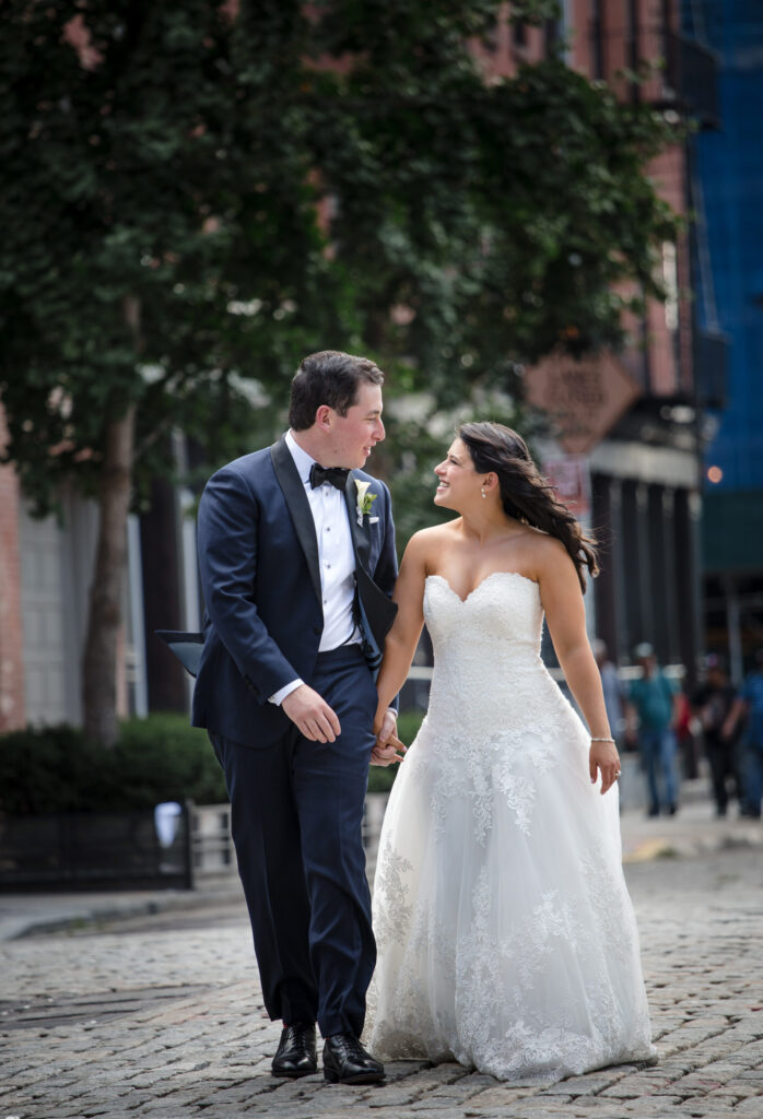 A bride and groom walking down a cobblestone street during their wedding at Pier Sixty.