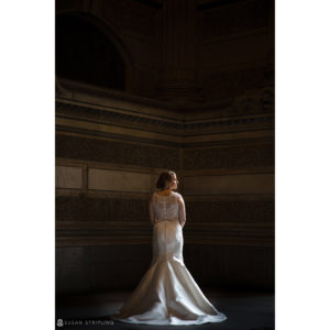 A wedding bride in a stunning wedding dress standing in an ornate room at Loews Hotel in Philadelphia.