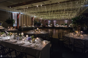A wedding reception at Pier Sixty, a breathtaking ballroom venue adorned with elegantly hanging lights from the ceiling.