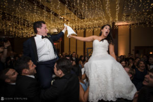 At a wedding reception at Pier Sixty, the bride and groom joyfully lift each other up in the air as they embrace.