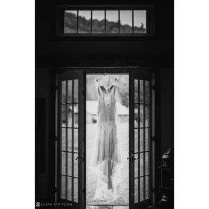 A black and white photo of a wedding dress hanging in a doorway at Riverside Farm, perfect for a summer wedding.