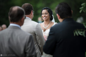 A bride smiles at her groom during a riverside farm wedding ceremony.