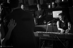 Black and white photo of a woman playing a piano in front of a group of people at the Gramercy Park Hotel.