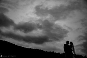 A bride and groom standing under a cloudy sky at their Riverside Farm summer wedding.