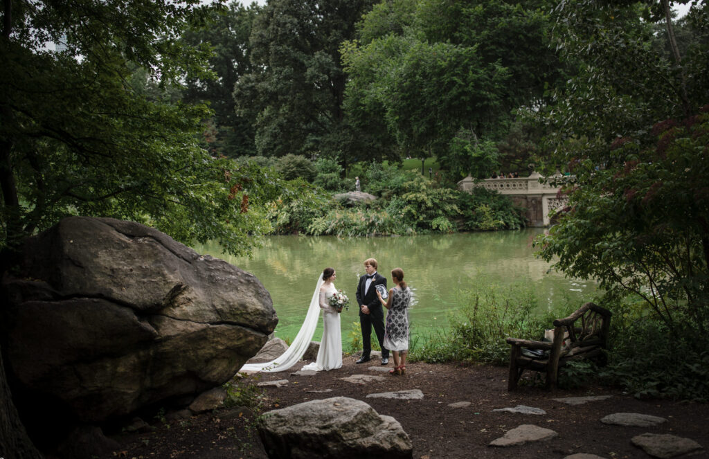 A bride and groom embracing each other in Central Park, with a serene pond as the backdrop for their intimate elopement ceremony.
