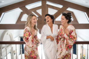 Three bridesmaids in floral robes laughing at a wedding in Bridgehampton, New York.