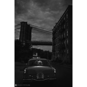 A black and white photo of a car in front of the Brooklyn Bridge.