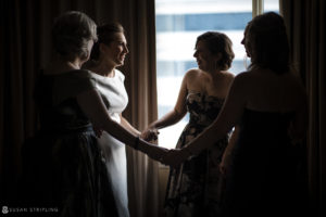 A bride and her bridesmaids are holding hands in front of a window at a wedding.
