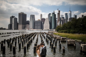 A wedding couple kisses in front of the Manhattan skyline at 1 Hotel Brooklyn Bridge.