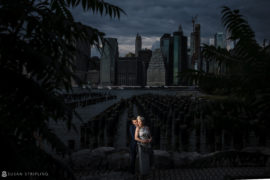 An elopement couple poses in front of a city skyline at the Brooklyn Bridge Park.