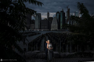 An elopement couple poses in front of a city skyline at the Brooklyn Bridge Park.