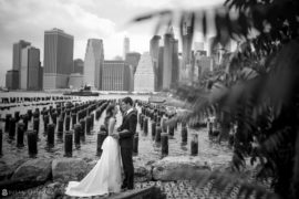 A bride and groom are posing in front of the stunning manhattan skyline, with the iconic One Hotel Brooklyn Bridge as their backdrop on their special wedding day.