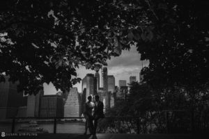 A black and white photo of a couple standing under a tree in Brooklyn Bridge Park.