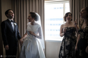 A bride and her bridesmaids are laughing in front of a window at their wedding at the Westin in Philadelphia.