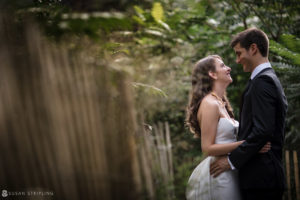 A bride and groom embracing at a wedding in front of a wooden fence.