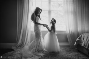 A bride and flower girl standing in front of a window in Bridgehampton, New York, on their wedding day.