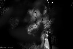 A bride and groom standing in the shadow of a castle at their wedding.