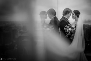 A bride and groom standing in front of a window in Central Park, embracing their elopement.