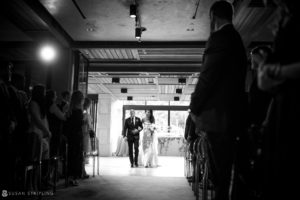 A black and white photo capturing the ethereal ambiance of a wedding at the Hotel Brooklyn Bridge, as a bride and groom elegantly walk down the aisle.