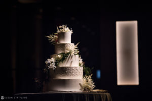 A white wedding cake sitting on a table in a dark room at the Hotel Brooklyn Bridge.