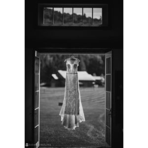 A black and white riverside farm wedding dress hanging from an open door.