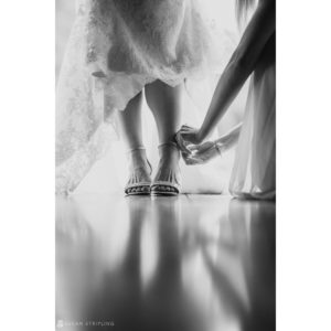 A bride is putting on her shoes at a riverside farm wedding in a black and white photo.