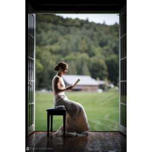 A riverside bride sitting in an open door reading a book at her farm wedding.