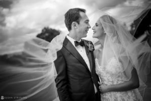 A black and white photo of a wedding couple kissing under a veil at the Sleepy Hollow Country Club.