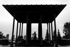 A silhouette of a bride standing under a rooftop gazebo.