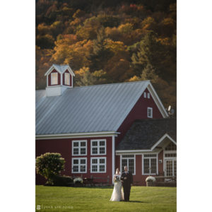A fall wedding with the bride and groom standing in front of a red barn at Riverside Farm.