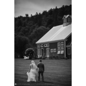 A riverside farm wedding with a bride and groom walking in front of a barn.