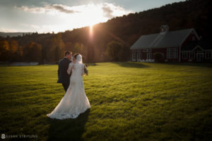 A bride and groom standing in a field at Riverside Farm with a barn in the background during their Fall Wedding.