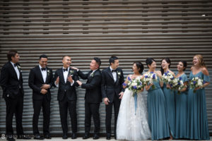 A group of bridesmaids and groomsmen in blue tuxedos celebrate on a Tribeca rooftop after a beautiful wedding ceremony.