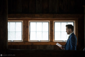 A man in a suit reading a book in a riverside barn.