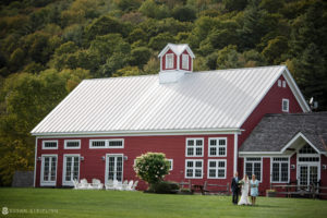 A riverside bride and groom standing in front of a red barn at their farm wedding.