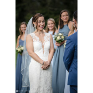 A bride smiles at her groom during a riverside farm wedding ceremony.