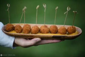 At a riverside farm wedding, a person holds a tray of delicious meatballs held by toothpicks.