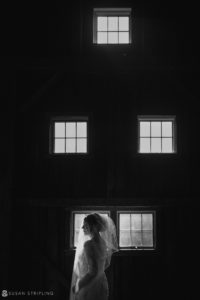 A bride standing in front of a window in Riverside Farm, embracing the ambiance of her fall wedding.