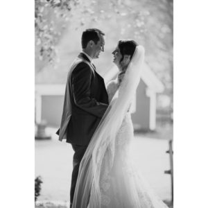 A black and white photo of a bride and groom celebrating their wedding in front of a barn at Riverside Farm during the fall season.