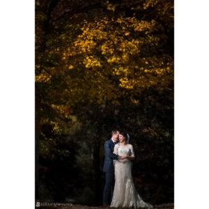 A bride and groom embracing in front of trees in the fall at Riverside Farm.