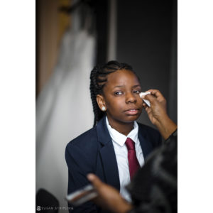 A young girl getting her makeup done at a wedding by a man in a suit at 501 Union.